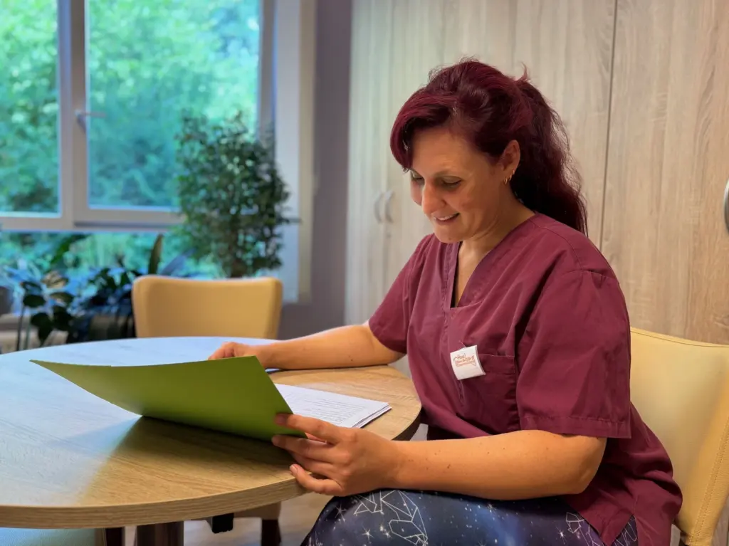 Pflegefachassistentin im Haus Tannenberg Gummersbach sitzt an einem Tisch und liest lächelnd in einer grünen Mappe.
