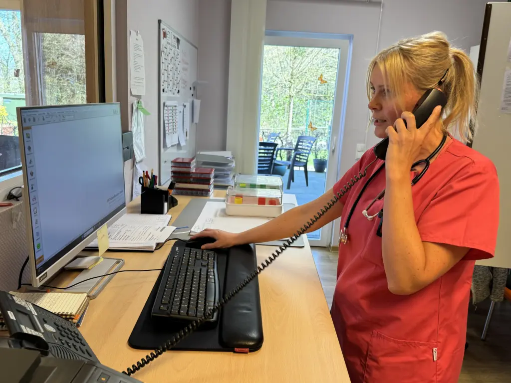 Pflegefachkraft im Haus Tannenberg Gummersbach steht an einem Schreibtisch, telefoniert und arbeitet gleichzeitig am Computer.
